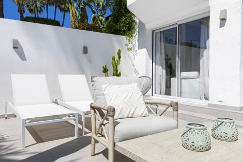 Modern Marbella townhouse patio with white loungers, rattan chair, cacti, and sliding glass doors overlooking garden