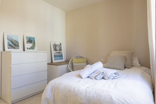 Bright bedroom at Marbella Home Rentals cottage with white bed, rolled towels, beige pillows, white dresser, and coastal