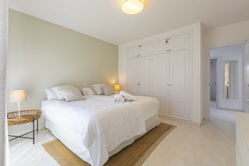 Bright modern master bedroom with white queen bed, built-in wardrobes, and cream décor at Marbella Home Rentals