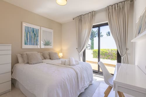 Bright modern bedroom in Marbella beachside townhouse with garden view patio doors, white furnishings, and neutral decor