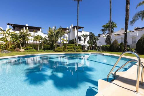 Crystal-blue resort pool with palm trees and white townhouses at Marbella Home Rentals, Guadalmina Baja