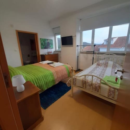 Comfortable beds with television, clothes rack, and bed side table | Welcome to Casa Rural "A Escola" – Your Tranquil Retreat in Pampilhosa da Serra
