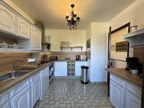 Modern kitchen in Locacharme cottage, Blois with white cabinetry, wooden countertops, and elegant chandelier
