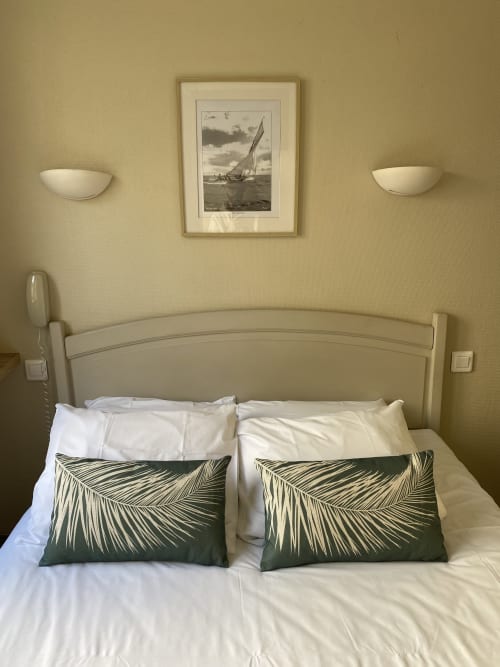 Elegant bedroom at Hôtel Maison Richet with cream headboard, patterned pillows, and sailboat artwork above bed