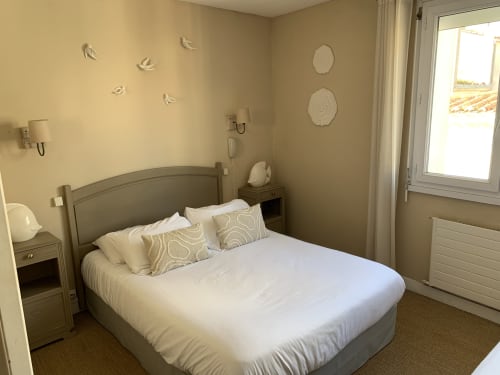Bright bedroom at Hôtel Maison Richet with double bed, beige walls, coastal decor, and garden views through glass doors