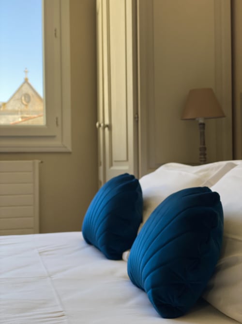 Elegant suite bedroom at Hôtel Maison Richet with blue pillows, white linens, and church view in Les Sables-d'Olonne