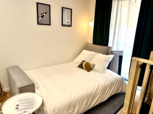Modern bedroom at Wellkhome Bordeaux with queen bed, gray headboard, white linens, city view, and minimalist wall art
