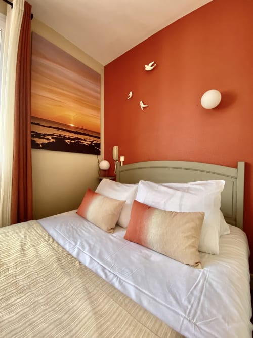 Bright single bedroom at Hôtel Maison Richet with terracotta accent wall, sunset artwork, and white bedding with accent