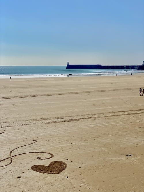 Sandy beach at Les Sables-d'Olonne with breakwater, heart drawing in sand, and visitors exploring the shoreline