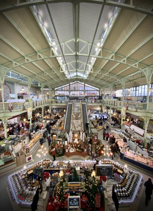 Interior of Les Sables-d'Olonne market hall with vendors, escalators, and glass roof structure