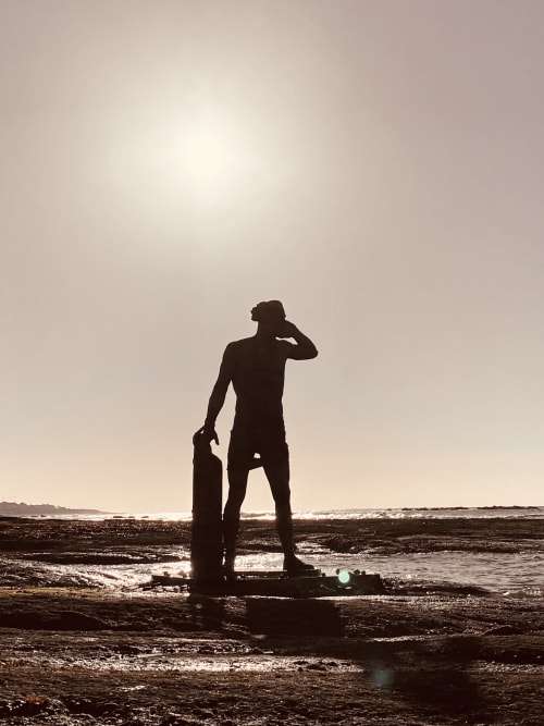 Surfer holding board at Les Sables-d'Olonne beach at sunset, silhouetted against ocean waves
