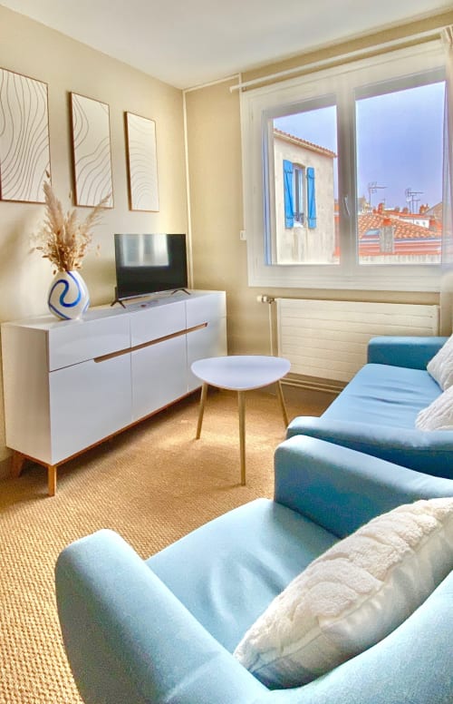 Modern suite at Hôtel Maison Richet with blue armchairs, white dresser, TV, and ocean view in Les Sables-d'Olonne
