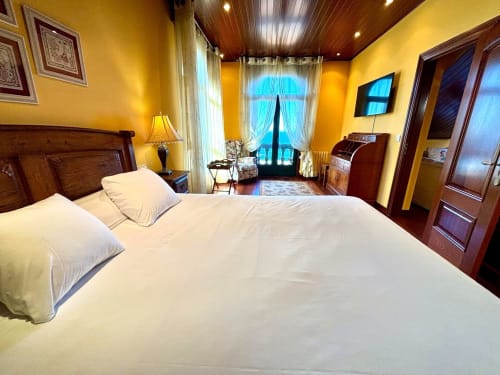 Dormitorio de lujo en villa de Baiona con paredes amarillas, vigas de madera, vistas al océano desde balcón y mobiliario elegante