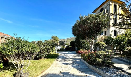 Entrada elegante de villa en Baiona con jardines cuidados, sendero arbolado y edificio de piedra tradicional con vistas al