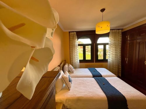 Amplio dormitorio en villa Vila Arume, Baiona, con camas gemelas, lámpara colgante amarilla y vistas al mar