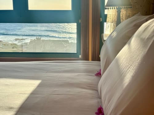 Lujosa habitación frente al mar en la villa Vila Arume, Baiona, con vistas al océano a través de amplios ventanales y ropa de cama blanca con detalles en rosa