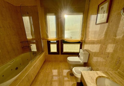 Baño lujoso en villa Vila Arume, Baiona con acabados en travertino, bañera spa y vistas al océano