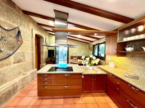 Cocina moderna con armarios de madera, isla de encimera de granito y vistas al mar en la villa Vila Arume en Baiona