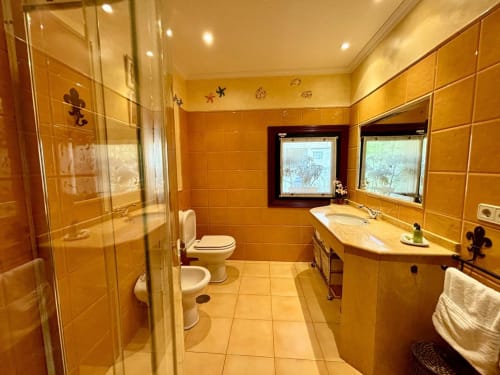 Lujoso baño en villa Vila Arume, Baiona, con azulejos dorados, cabina de ducha cristal, doble lavabo y ventanas