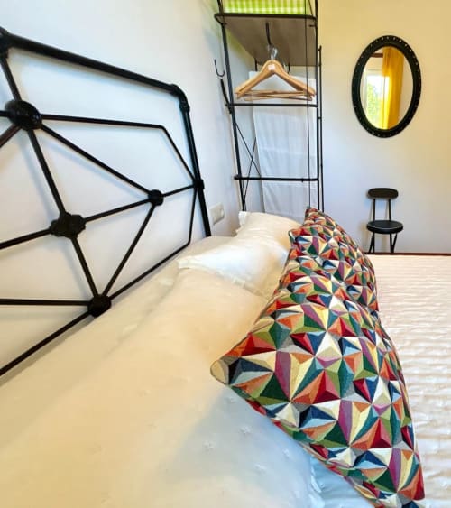 Dormitorio moderno de la casa rural Casa Caeiro en Baiona con almohada geométrica colorida, cabecero geométrico negro y perchero de madera.