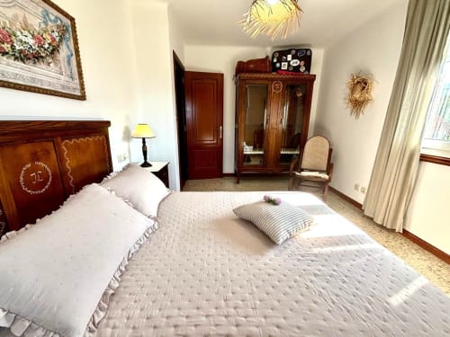 Amplio dormitorio con cabecero de madera, ropa de cama blanca y vistas al mar cerca de Baiona. Casa Caeiro con jardín y acceso a piscina.