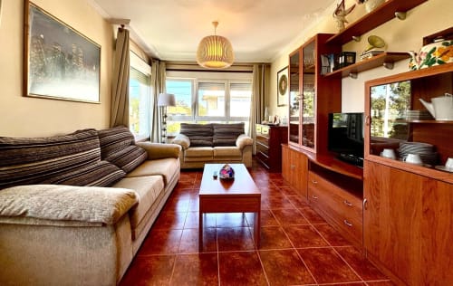 Luminoso salón de la casa rural Casa Caeiro en Baiona con sofás rayados, suelos de baldosa roja, muebles de madera, TV y vistas al mar