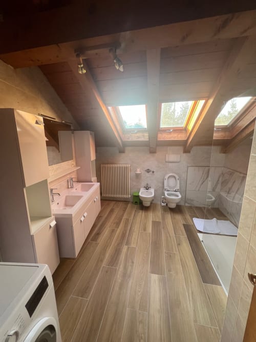 Spacious attic bathroom at Appartamento Giustina with dual sinks, skylights, wooden flooring, and mountain views