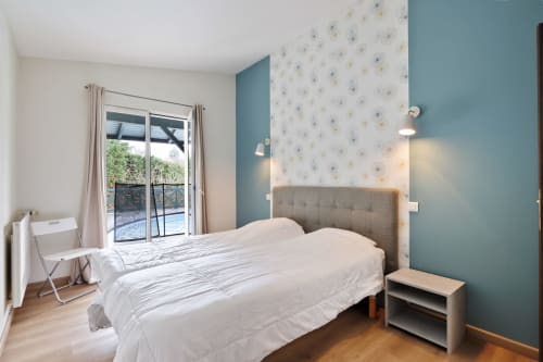 Dormitorio luminoso con cama doble, puertas con vistas a la piscina y pared de acento azul verdoso en Villa Ongizatea, Urrugne