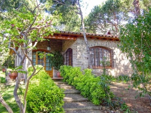 Maison de pierre avec porte en bois et volets, entourée de jardins luxuriants et d'arbres à Finques Garcia Enrich