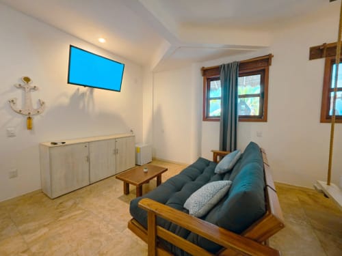 Acogedora habitación del hotel 40 Cañones con sofá azul, muebles de madera, TV y vistas al patio desde las ventanas en Mahahual