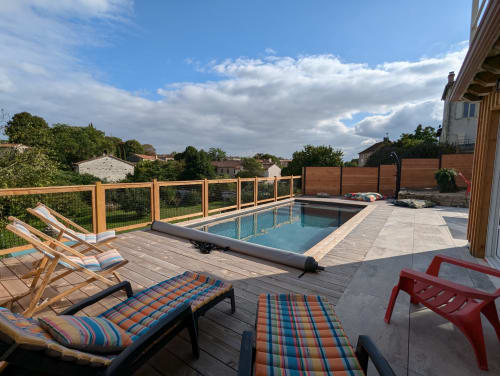 Espace piscine du gîte de charme La Grange des Colporteurs avec terrasse en bois, transats colorés, chaises pliantes et vue sur la campagne charentaise. Lieu idéal pour se détendre en famille ou entre amis en Nouvelle-Aquitaine.