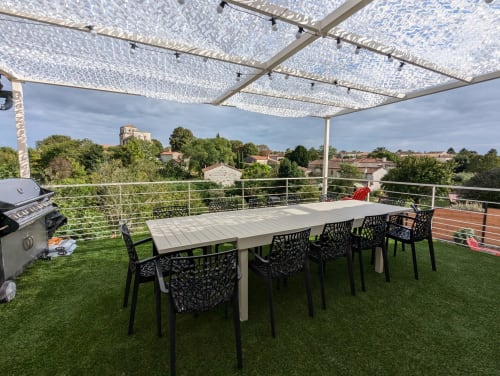 Terrasse du gîte La Grange des Colporteurs avec table pour 8 personnes, gazon synthétique, barbecue et vue sur la campagne charentaise. Espace convivial pour repas en plein air en famille ou entre amis.