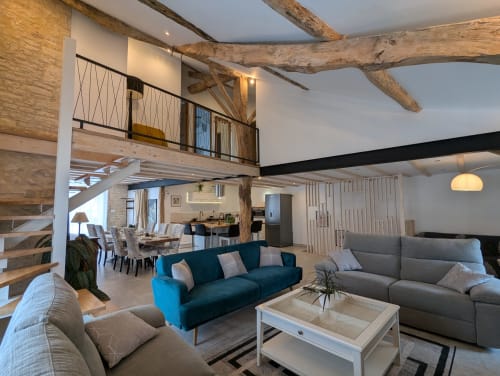 Espace de vie du gîte La Grange des Colporteurs avec mezzanine, poutres apparentes, murs en pierre, cuisine moderne, et coin salon cosy. Gîte spacieux et lumineux en Charente, idéal pour des vacances en famille.