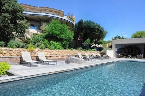 Piscine de la Villa Marina Di Cavu avec chaises longues, terrasse en pierre et maison moderne surplombant le jardin à Bonifacio