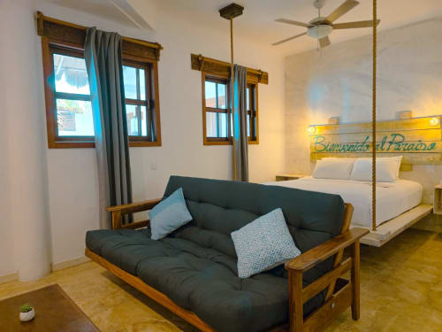 Habitación moderna del Hotel 40 Cañones en Mahahual con sofá futón, cama dosel, ventanas de madera y ventilador de techo