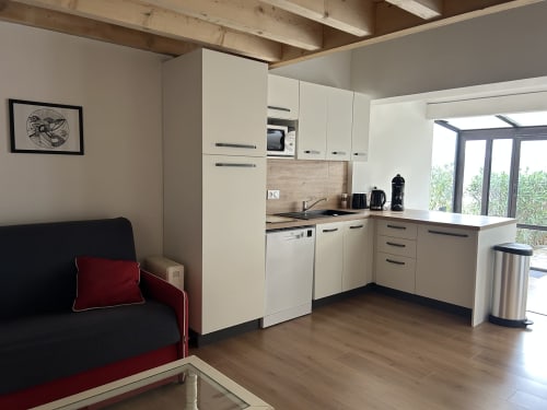 Cuisine et séjour modernes au Mazet Cavalaire : mobilier blanc, poutres en bois, canapé noir et vue sur mer