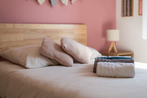 Chambre de la Maison Love Lane avec oreillers moelleux, serviettes pliées sur le lit et mur d'accent rose à Cagnes-sur-Mer