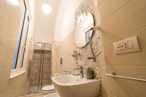 Bagno moderno con piastrelle beige, parete decorativa con motivi, lavabo bianco, doccia e asciugacapelli a Le Boutique