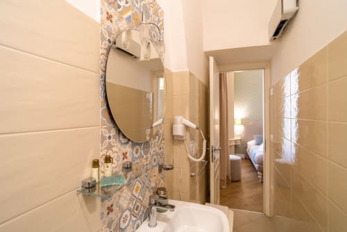 Bagno moderno a Le Boutique del Centro Napoli con specchio rotondo, piastrelle decorative e lavabo con amenities
