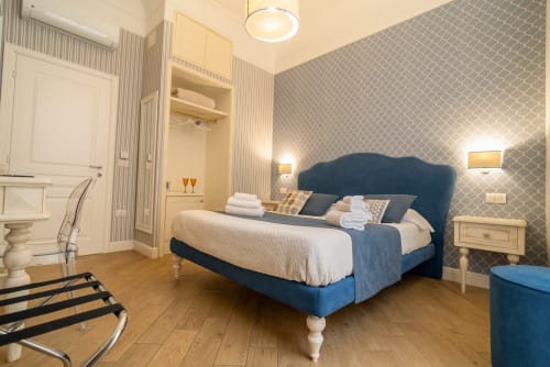 Camera matrimoniale elegante presso Le Boutique del Centro Napoli con letto imbottito blu, carta da parati decorativa e bagno ensuite