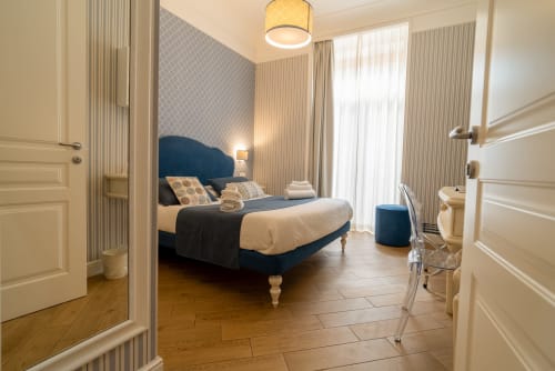 Elegante camera doppia presso Le Boutique del Centro a Napoli con letto in velluto blu, arredi color crema e balcone con vista sulla città