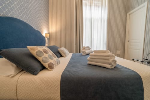 Elegante camera matrimoniale a Le Boutique del Centro Napoli con testata blu, biancheria color crema e tende con vista sulla città