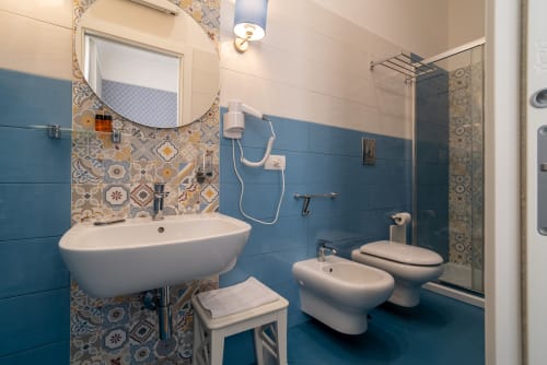 Bagno moderno con piastrelle blu, dettagli decorativi a motivi, lavabo bianco, bidet e wc presso Le Boutique del Centro, Napoli