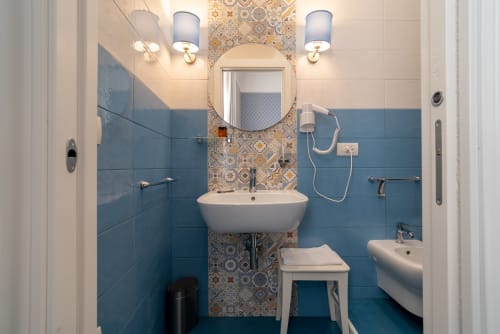 Bagno moderno con piastrelle blu presso Le Boutique del Centro a Napoli, specchio rotondo, doppio lavabo e parete con motivi decorativi