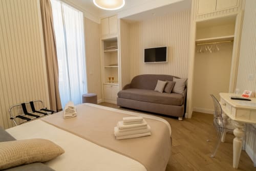 Camera Triple Esecutiva presso Le Boutique del Centro a Napoli con letto, divano marrone, scrivania, TV e arredamento color crema