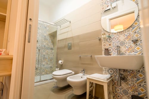 Bagno moderno a Le Boutique del Centro Napoli con piastrelle decorate, doccia freestanding, wc, bidet e lavabo con specchio