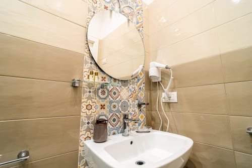 Bagno moderno all'hotel Le Boutique del Centro di Napoli con rivestimento decorativo in piastrelle, specchio rotondo, lavabo bianco e asciugacapelli