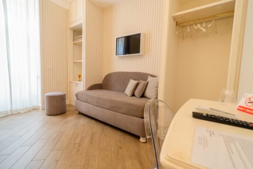 Camera esecutiva moderna a Le Boutique del Centro Napoli con divano beige, scrivania, TV e pavimentazione in legno
