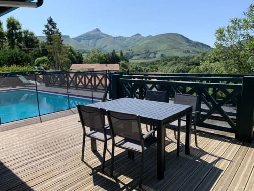 Terrasse avec table à manger et chaises face à la piscine bleue, aux montagnes et à la vallée verdoyante de la Villa Ongizatea, Urrugne