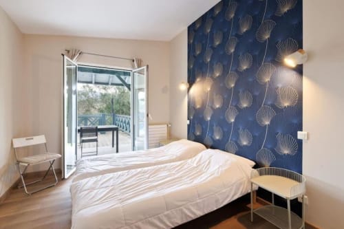 Modern bedroom with blue shell-patterned accent wall, white bed, glass doors to mountain terrace at Villa Ongizatea cottage